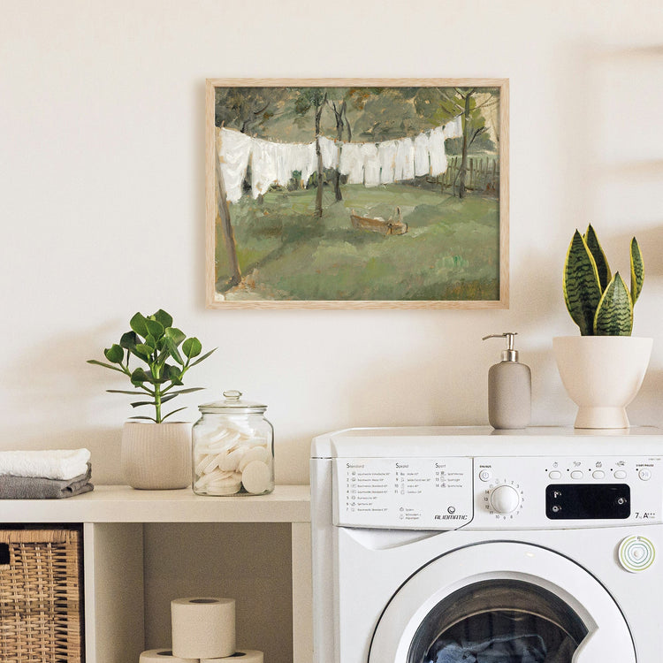 Framed vintage laundry room sketch art print featuring a woman washing clothes, styled above a washing machine with folded towels and a wicker basket.