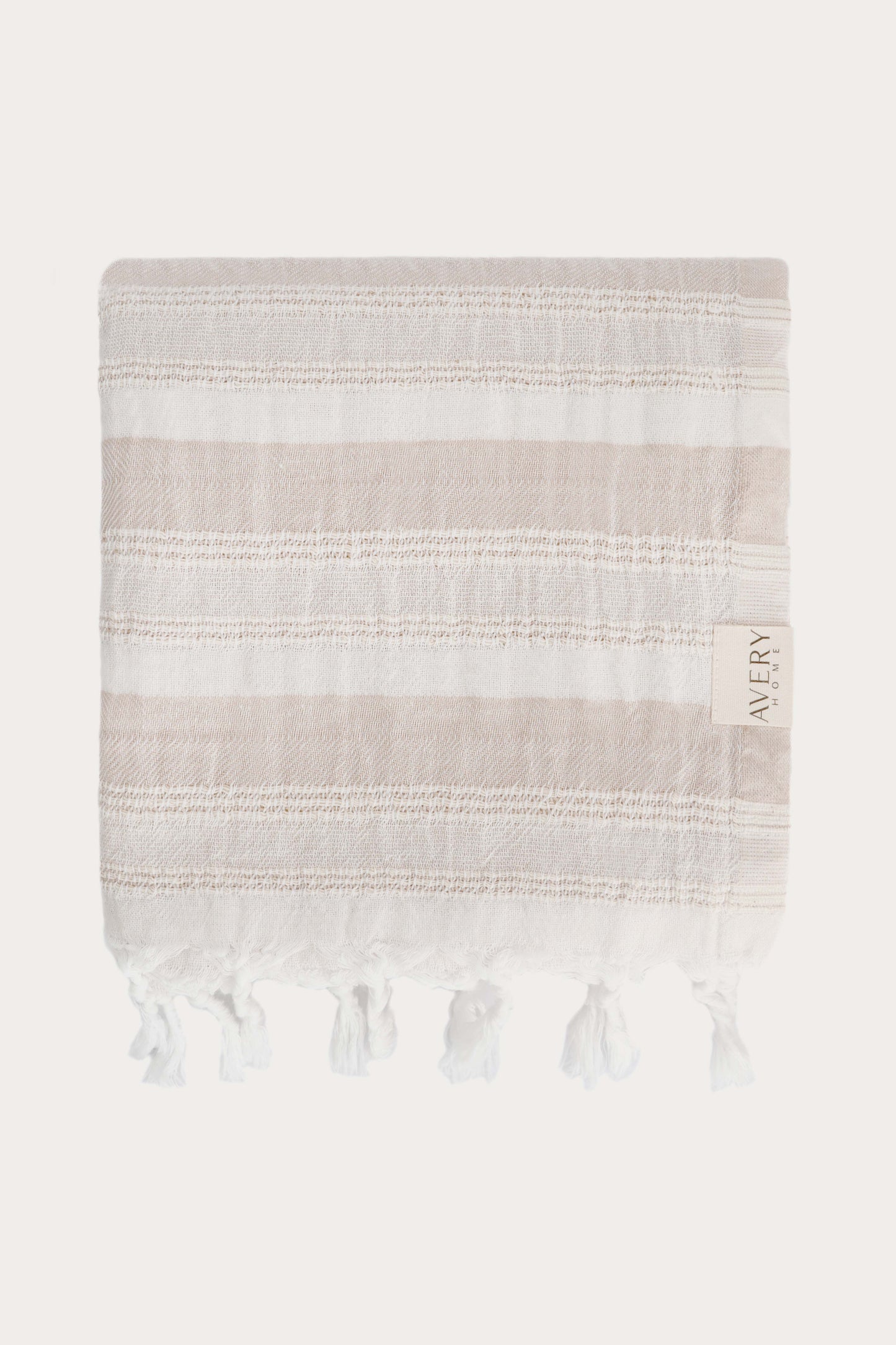Avery Home Formentera peshtemal folded in beige and white herringbone weave luxury Turkish hammam towel with hand-knotted tassel fringe, fast-drying and lightweight