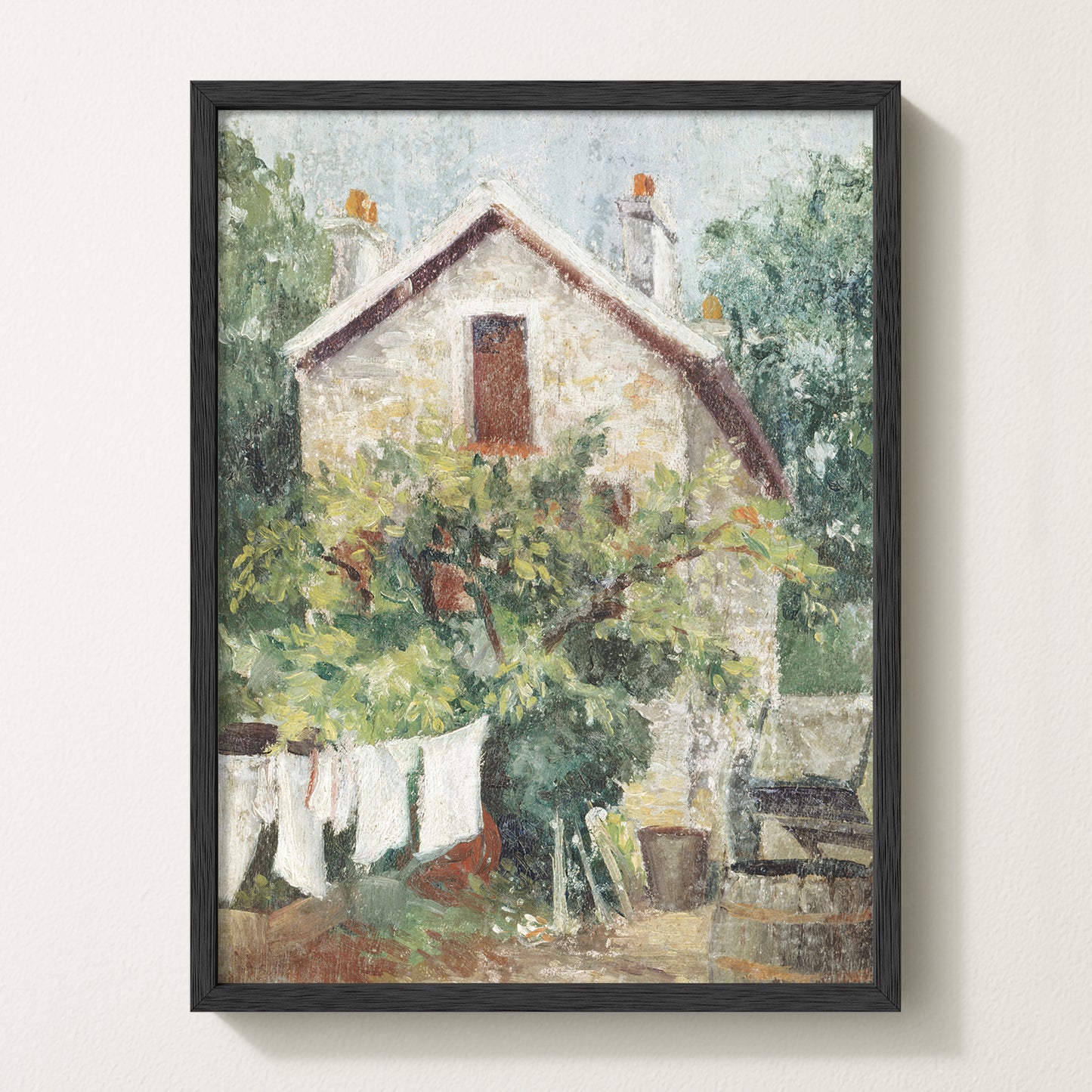 Framed vintage cottage art print featuring a stone house, lush greenery, and white laundry hanging on a clothesline in the garden.