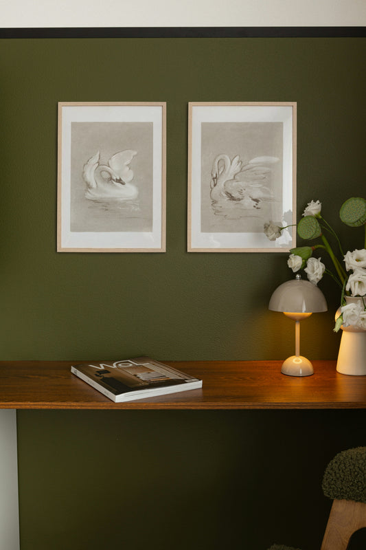 Framed vintage swan artwork styled on a deep green wall above a wooden console with a vase and decorative objects.