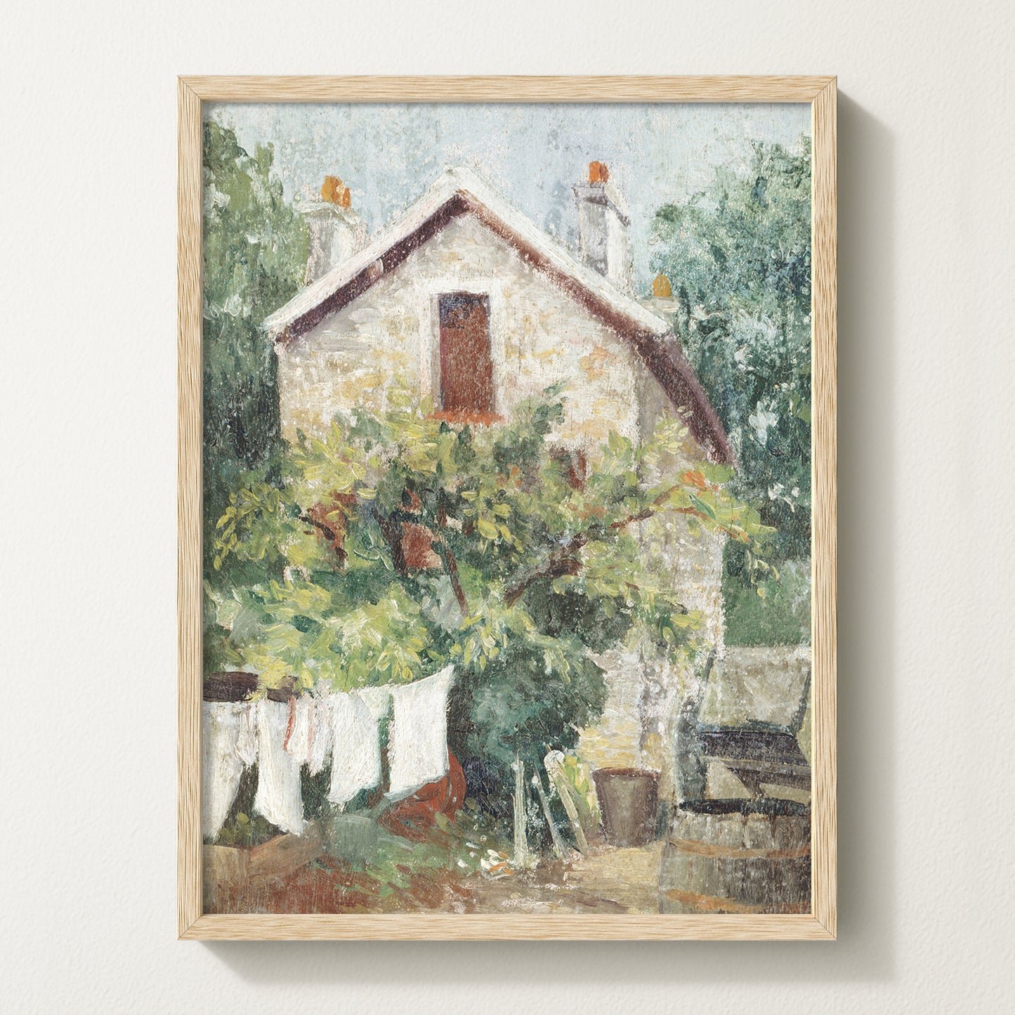 Framed vintage cottage art print featuring a stone house, lush greenery, and white laundry hanging on a clothesline in the garden