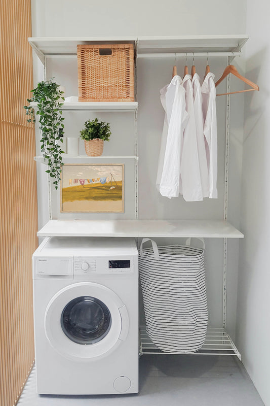 Vintage laundry room wall art above a washing machine in a modern farmhouse laundry room with neutral decor and framed countryside landscape print.