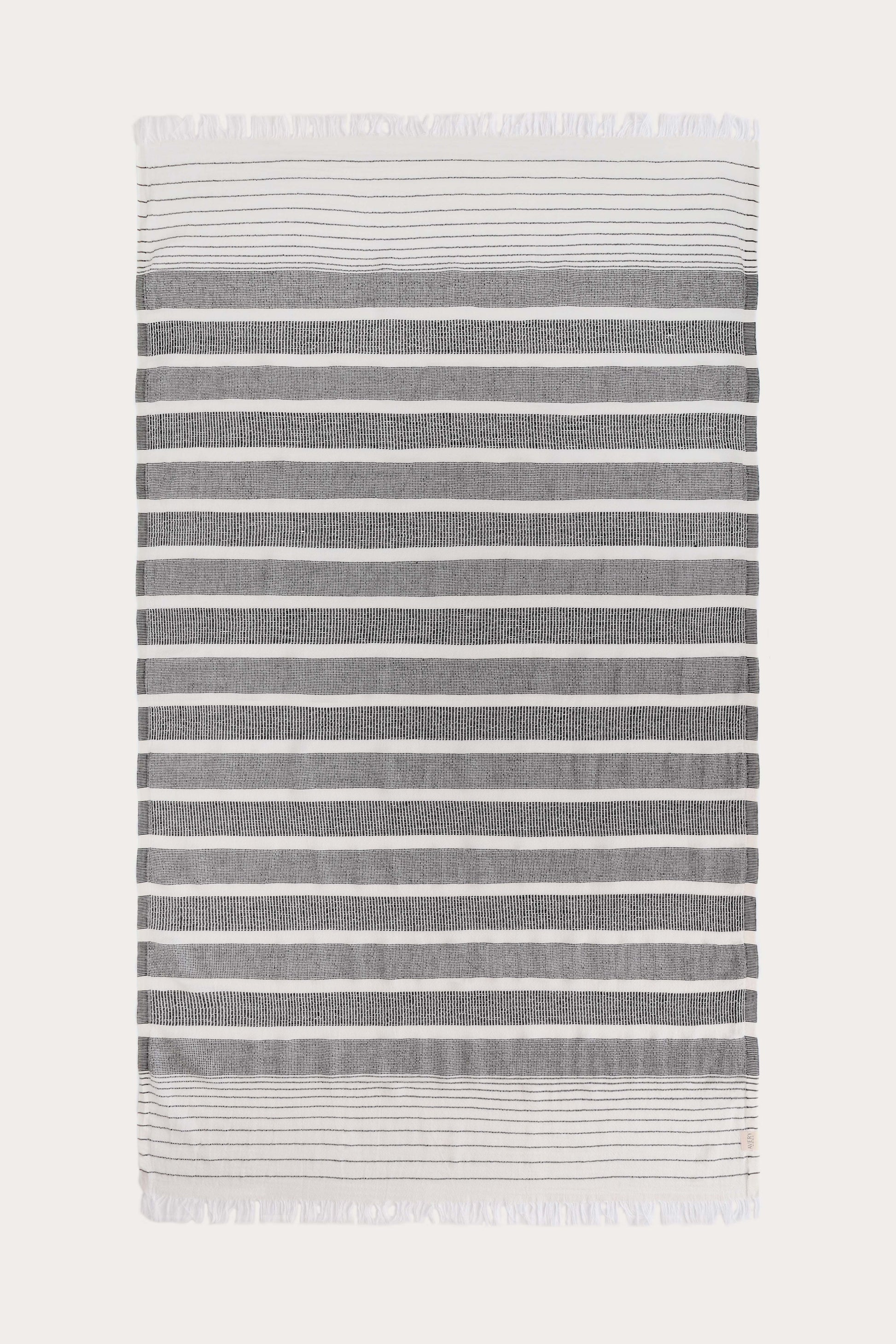 Avery Home black and white stripe peshtemal laid flat, full view of sustainable Turkish towel woven from cotton, recycled cotton and recycled polyester, with tassel fringe