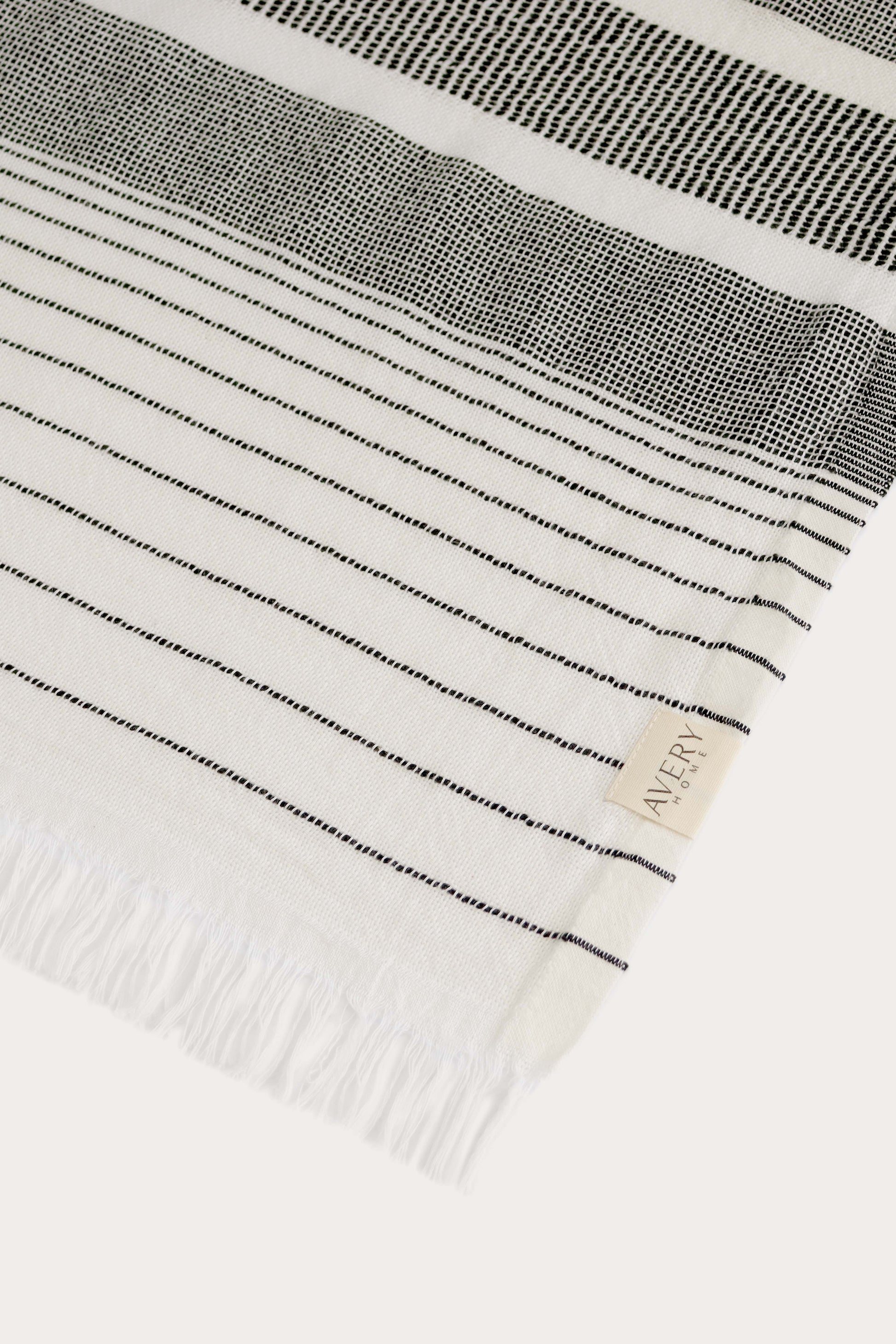 Close-up of Avery Home black and white stripe peshtemal showing open-weave texture and woven label, eco-friendly Turkish hammam towel in recycled cotton blend
