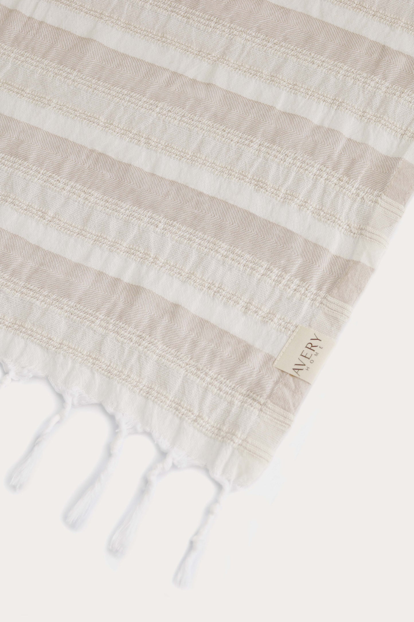 Close-up of Avery Home Formentera beige and white peshtemal showing herringbone weave texture and woven label, premium Turkish cotton hammam towel