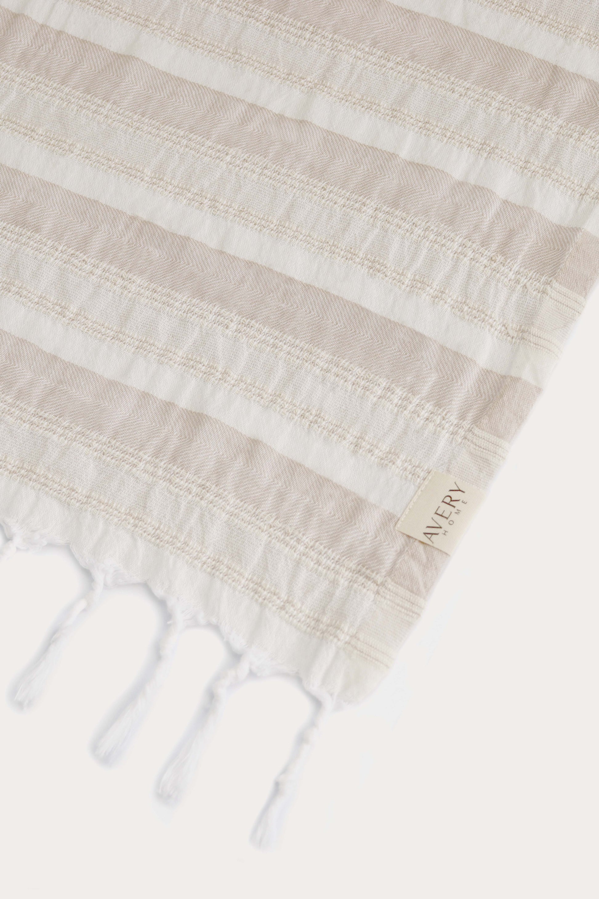 Close-up of Avery Home Formentera beige and white peshtemal showing herringbone weave texture and woven label, premium Turkish cotton hammam towel
