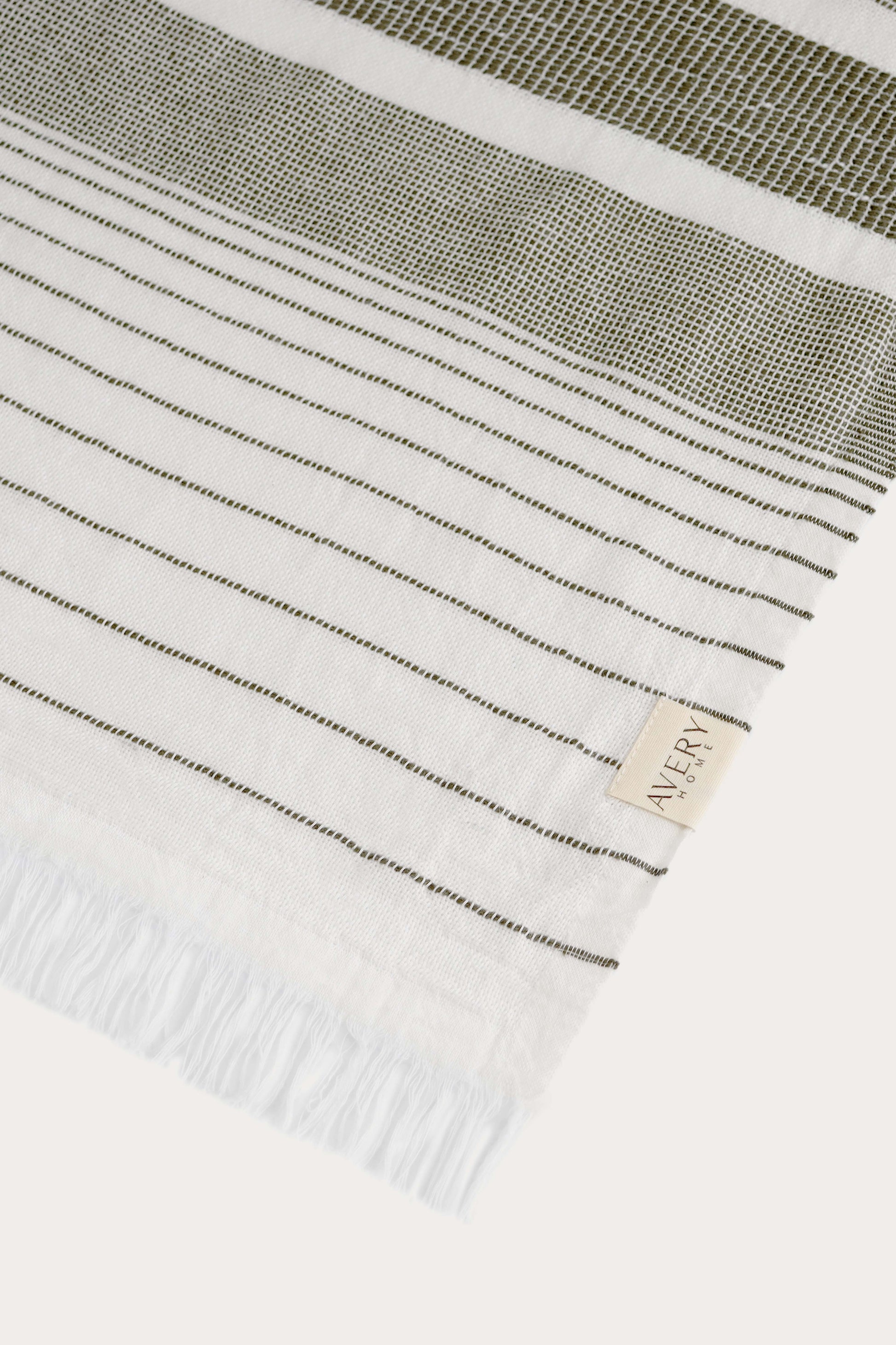 Close-up of Avery Home green stripe peshtemal showing open-weave texture and woven label, eco-friendly Turkish hammam towel in recycled cotton blend