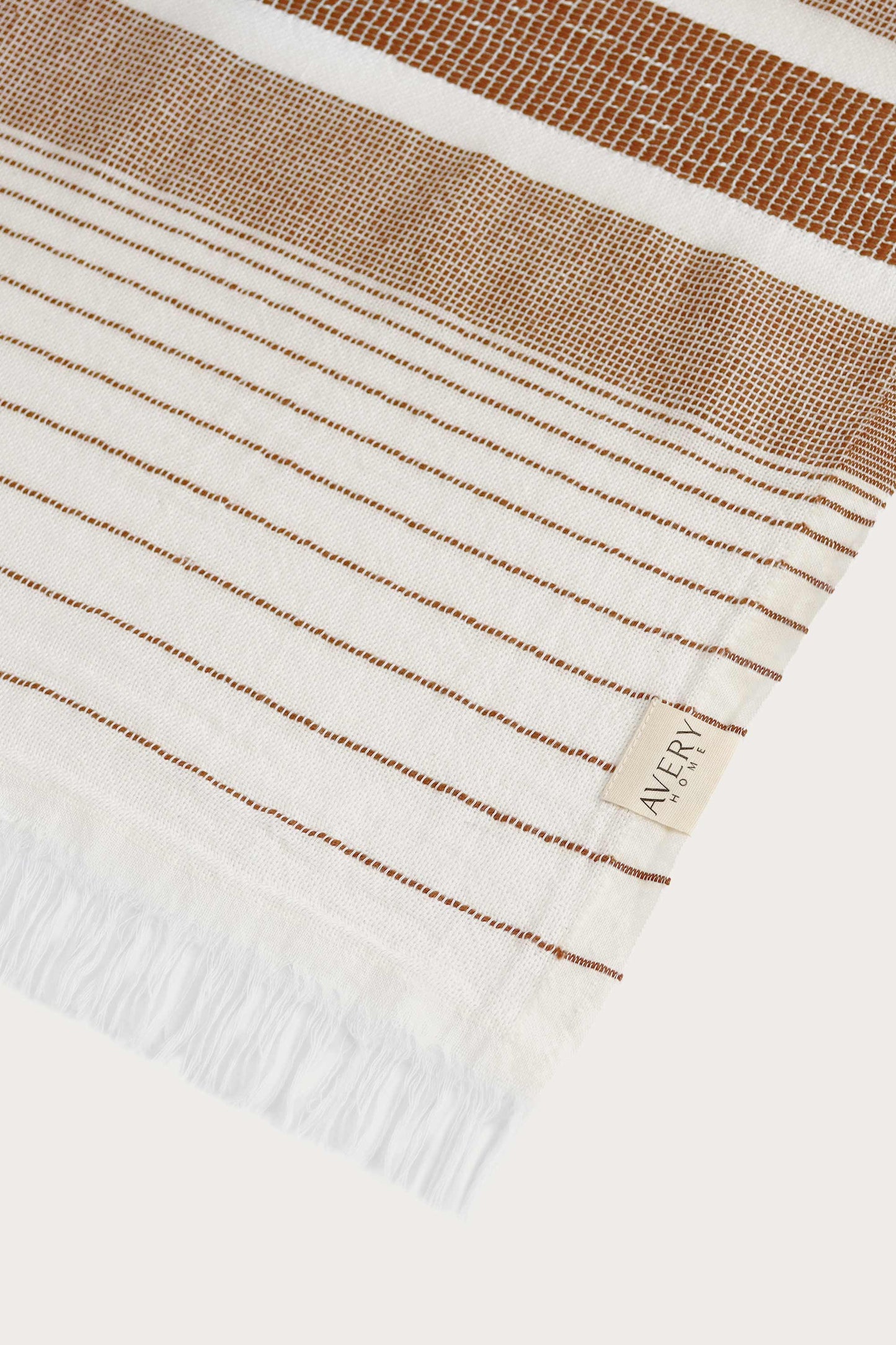 Close-up of Avery Home terracotta stripe peshtemal showing open-weave texture and woven label, eco-friendly Turkish hammam towel in recycled cotton blend