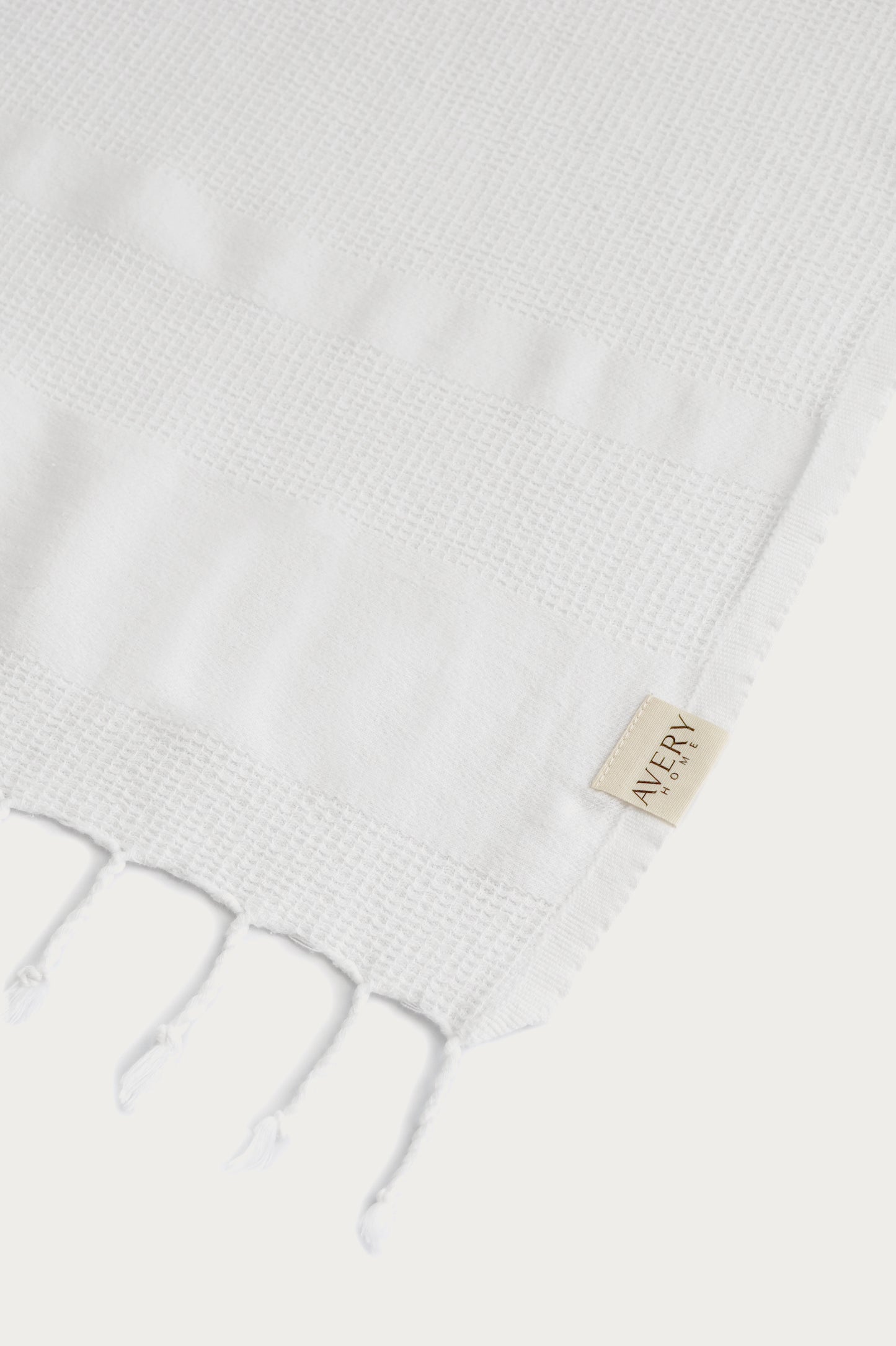 Close-up of hand-knotted tassel fringe and waffle weave texture on Avery Home white Turkish peshtemal – spa-quality hammam towel