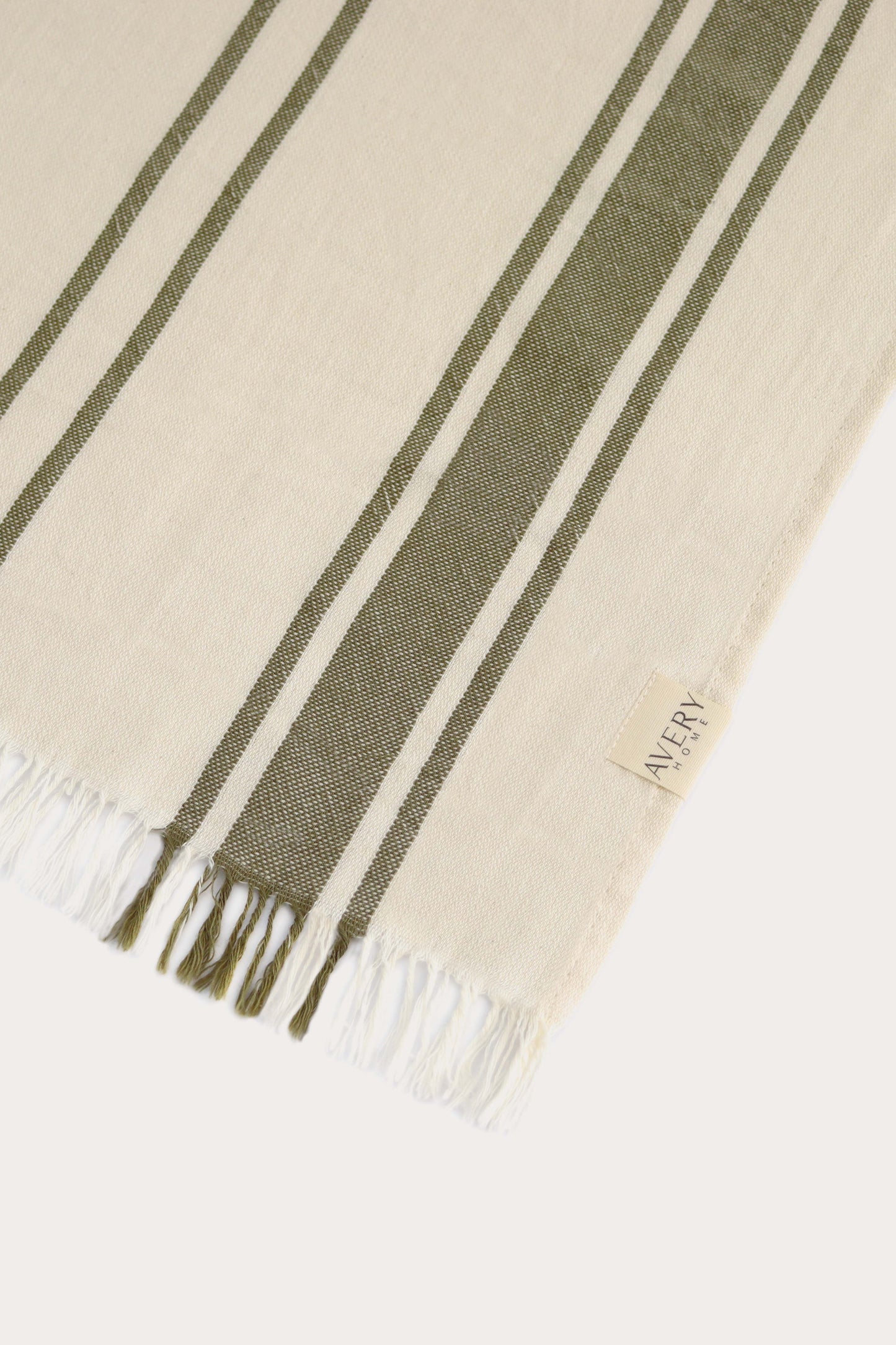 Close-up of green and beige Amalfi Turkish towel showing cabana stripe pattern, 100% cotton flat weave texture and fringe by Avery Home.
