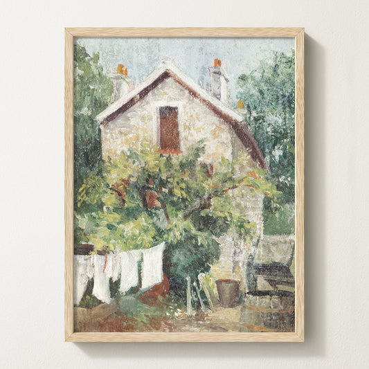 Framed vintage cottage art print featuring a stone house, lush greenery, and white laundry hanging on a clothesline in the garden