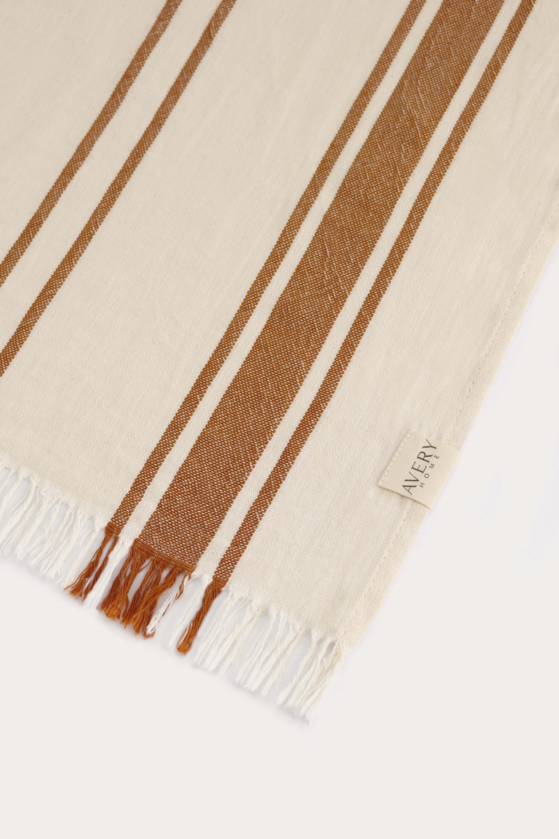 Close-up of orange and beige Amalfi Turkish towel showing cabana stripe pattern, 100% cotton flat weave texture and fringe by Avery Home.
