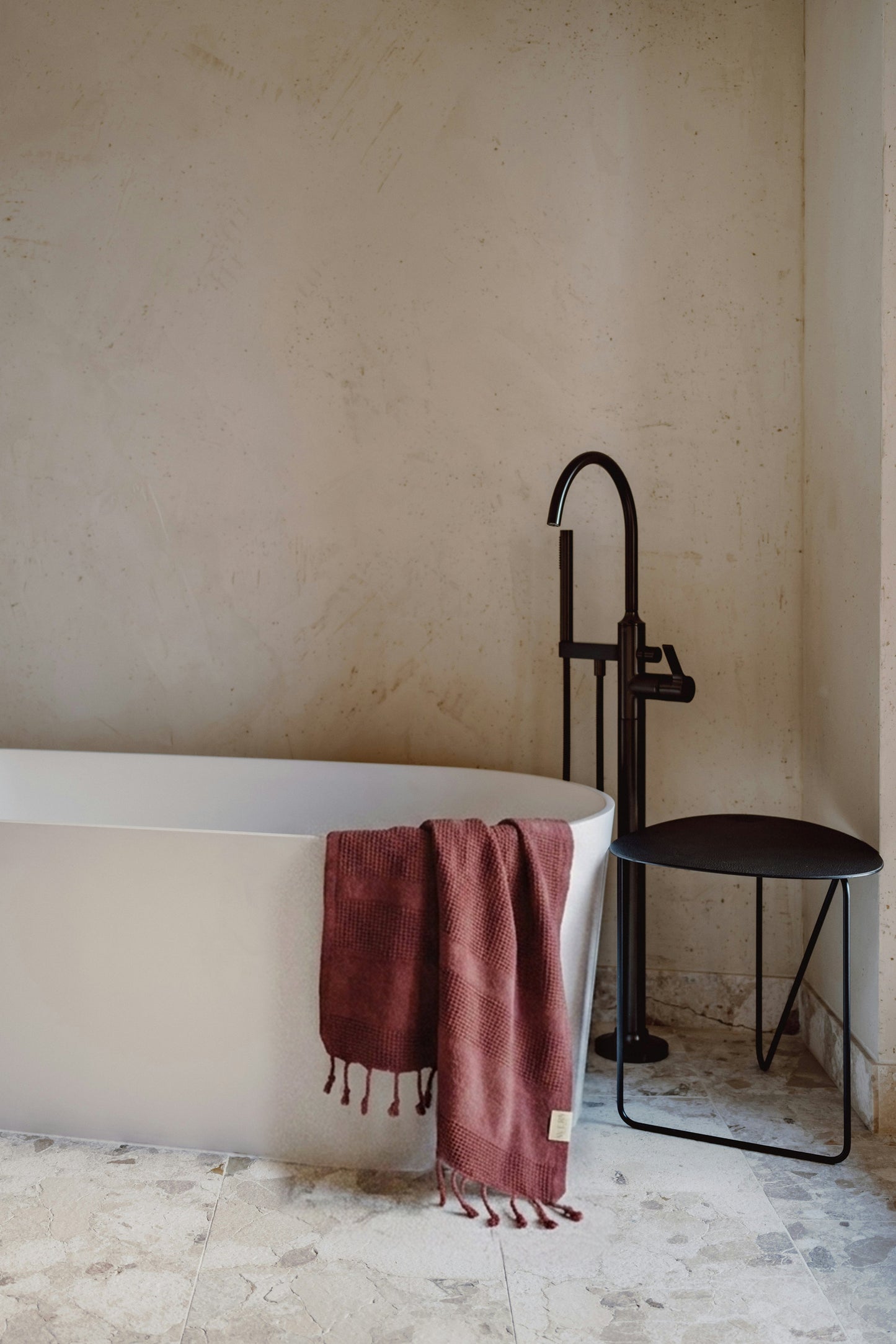 Burgundy waffle Turkish towel hanging in a minimalist marble bathroom with black fixtures and natural light by Avery Home.