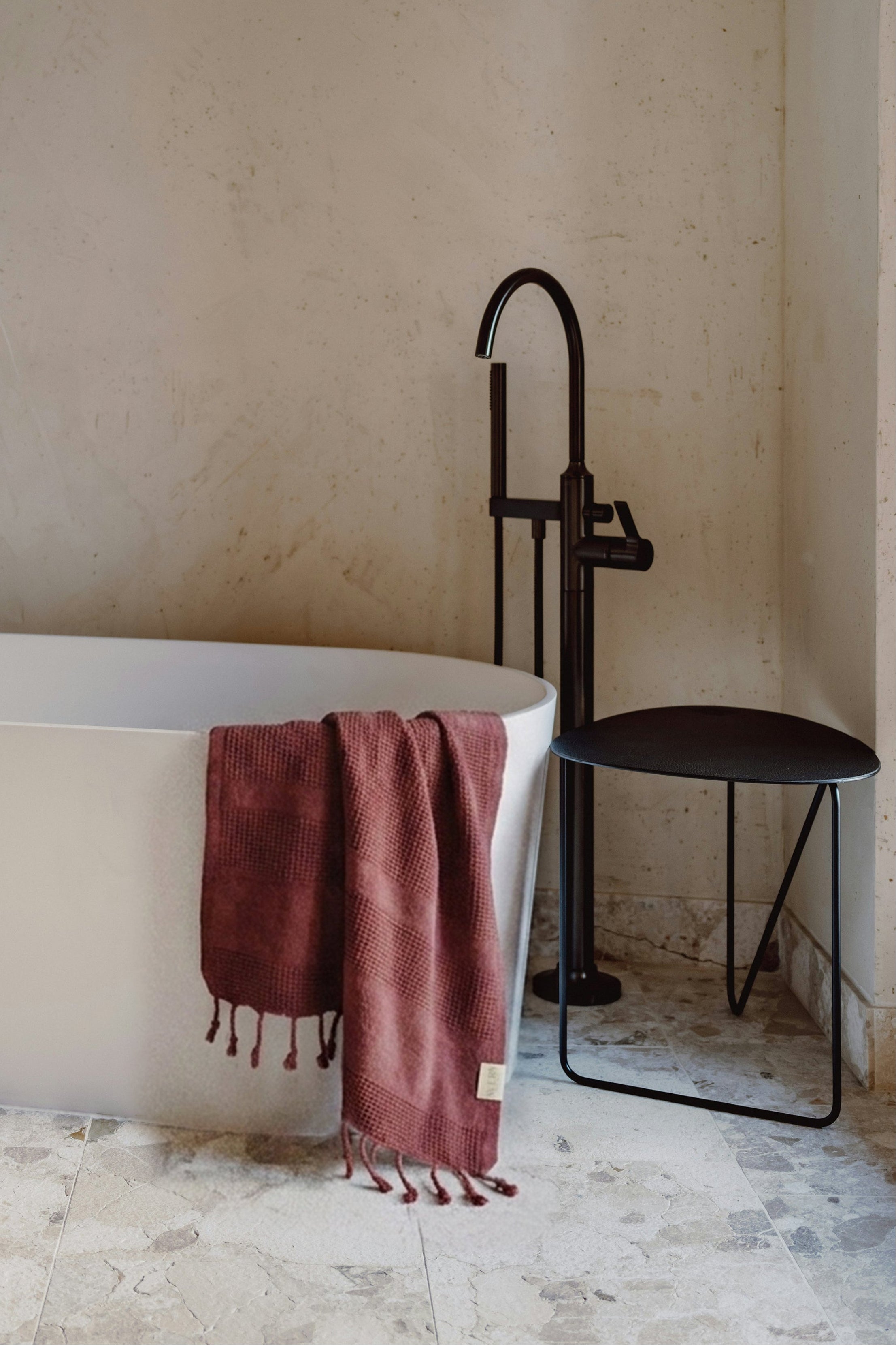 Burgundy waffle Turkish towel hanging in a minimalist marble bathroom with black fixtures and natural light by Avery Home.