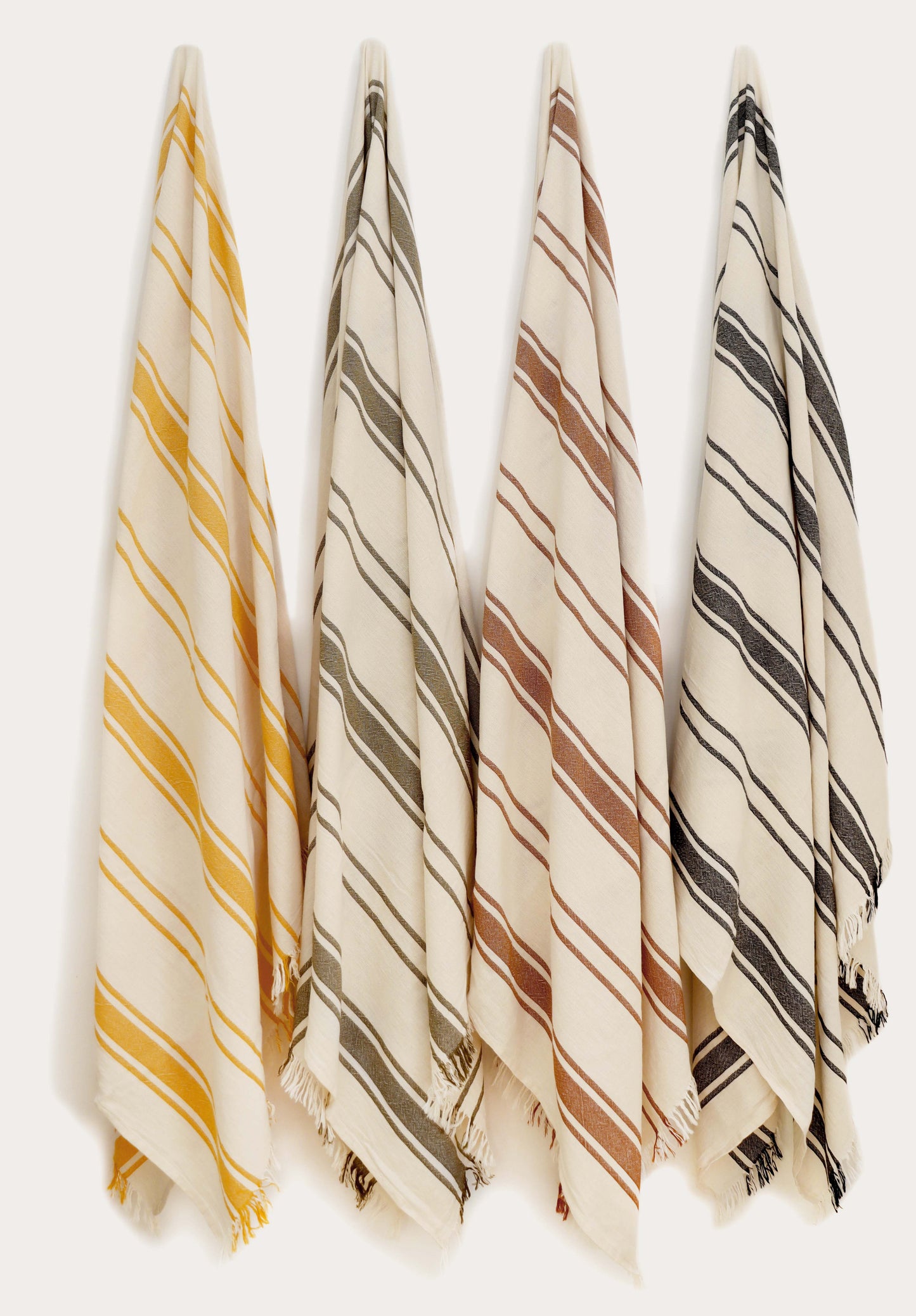 Collection of four striped Turkish cotton towels in yellow, green, terracotta, and black hanging on wall hooks. Lightweight, absorbent, quick-drying Turkish towels for beach, pool, bath, travel, and everyday home use by Avery Home.