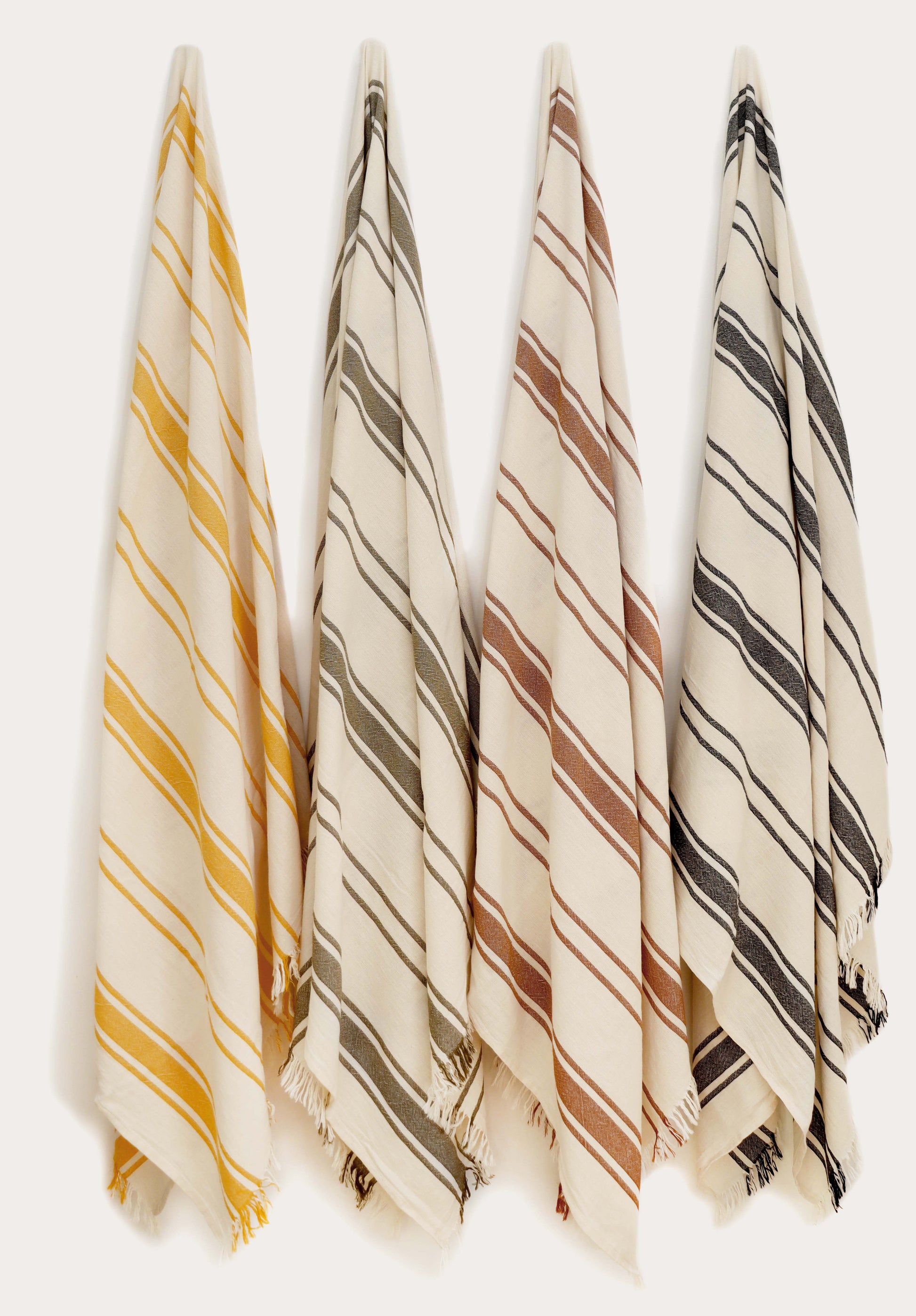 Collection of four striped Turkish cotton towels in yellow, green, terracotta, and black hanging on wall hooks. Lightweight, absorbent, quick-drying Turkish towels for beach, pool, bath, travel, and everyday home use by Avery Home.