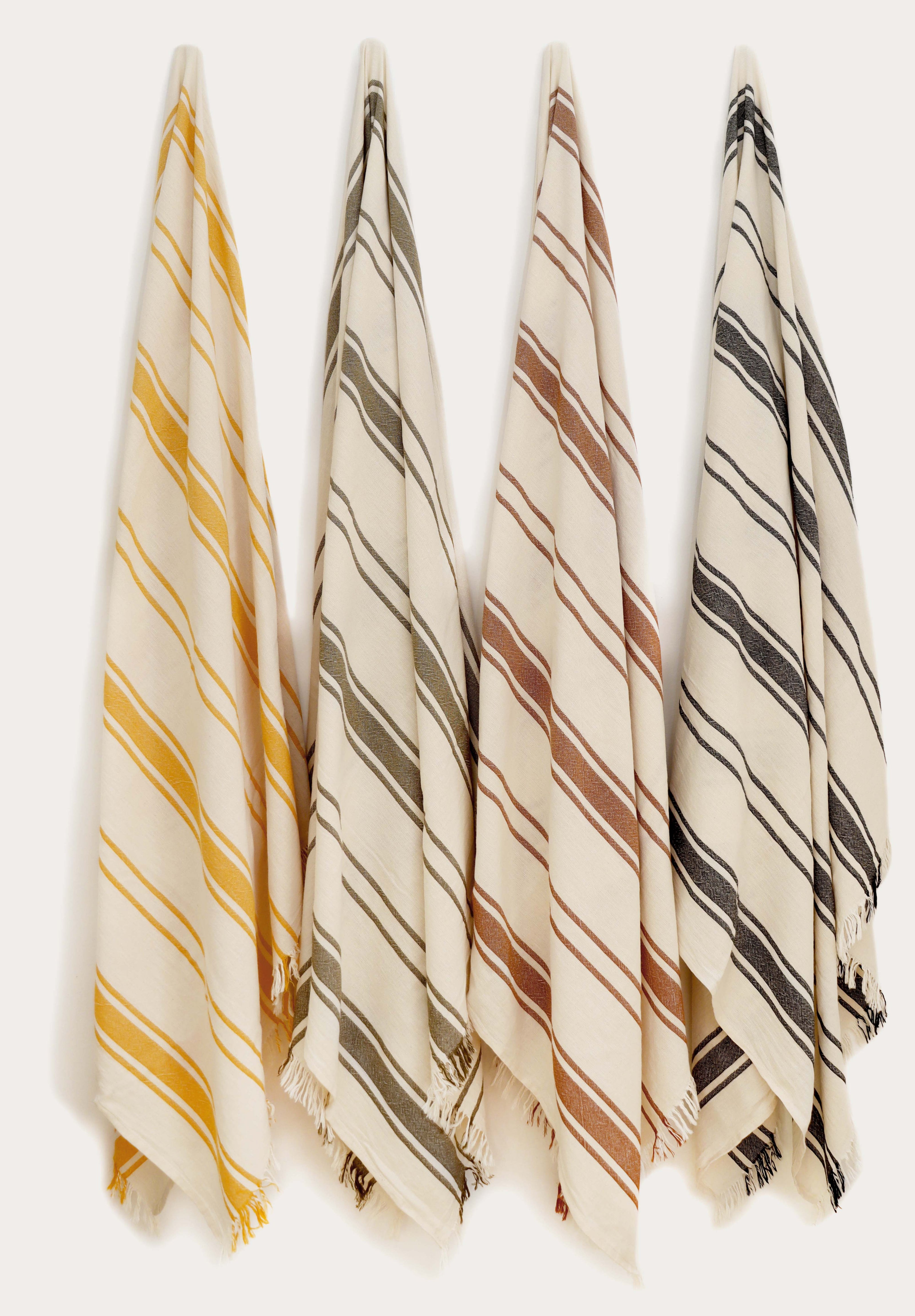 Collection of four striped Turkish cotton towels in yellow, green, terracotta, and black hanging on wall hooks. Lightweight, absorbent, quick-drying Turkish towels for beach, pool, bath, travel, and everyday home use by Avery Home.