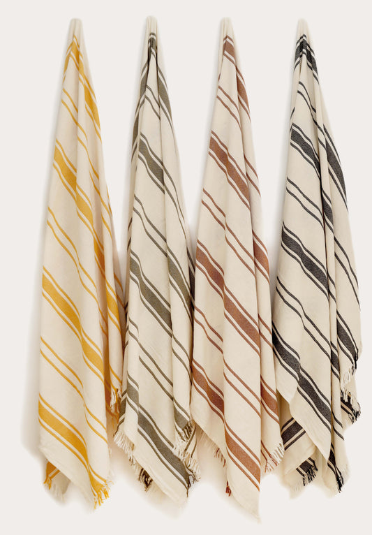 Collection of four striped Turkish cotton towels in yellow, green, terracotta, and black hanging on wall hooks. Lightweight, absorbent, quick-drying Turkish towels for beach, pool, bath, travel, and everyday home use by Avery Home.