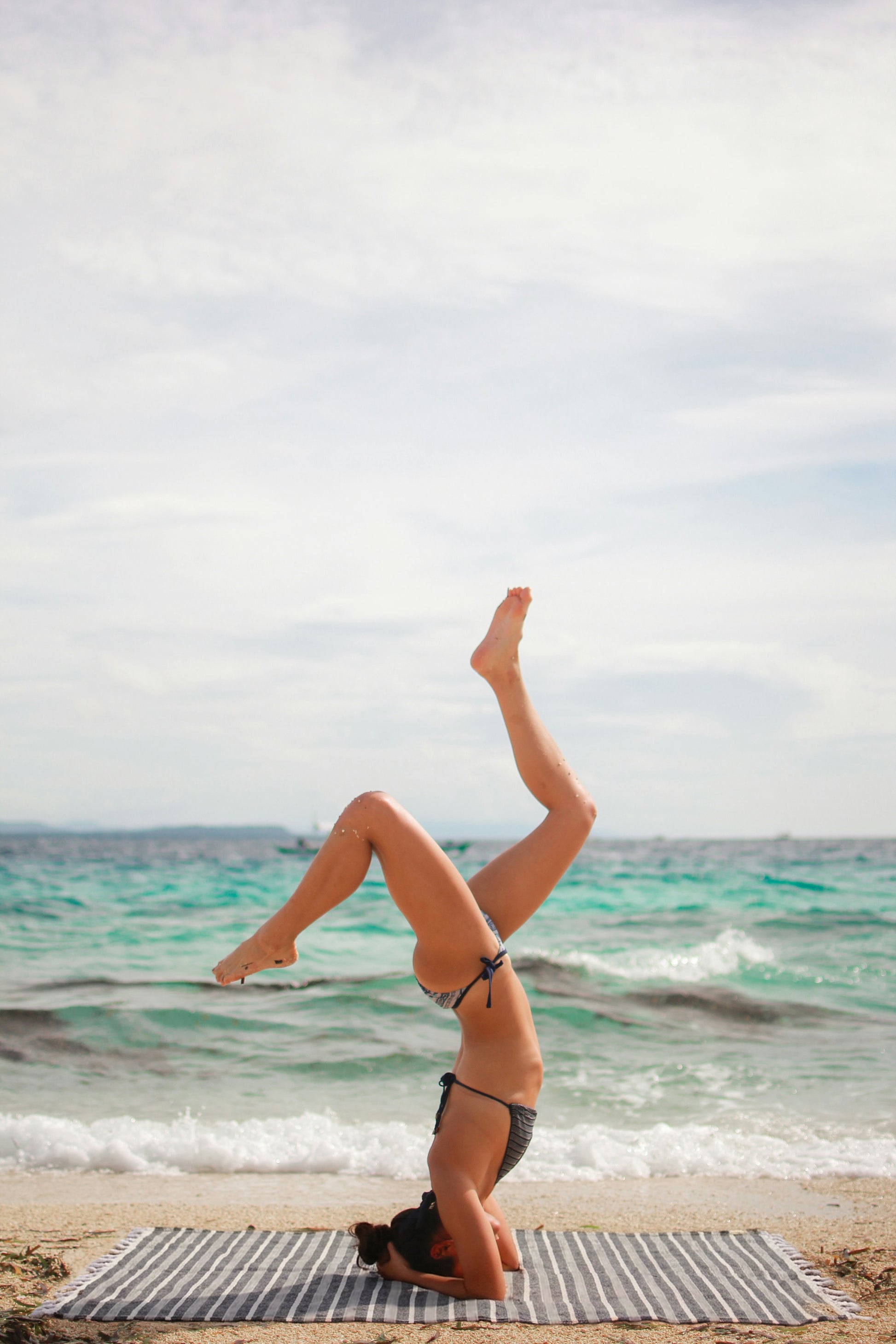 Woman practicing yoga headstand pose on a Turkish beach towel by the ocean, featuring a lightweight quick-dry travel towel by Avery Home