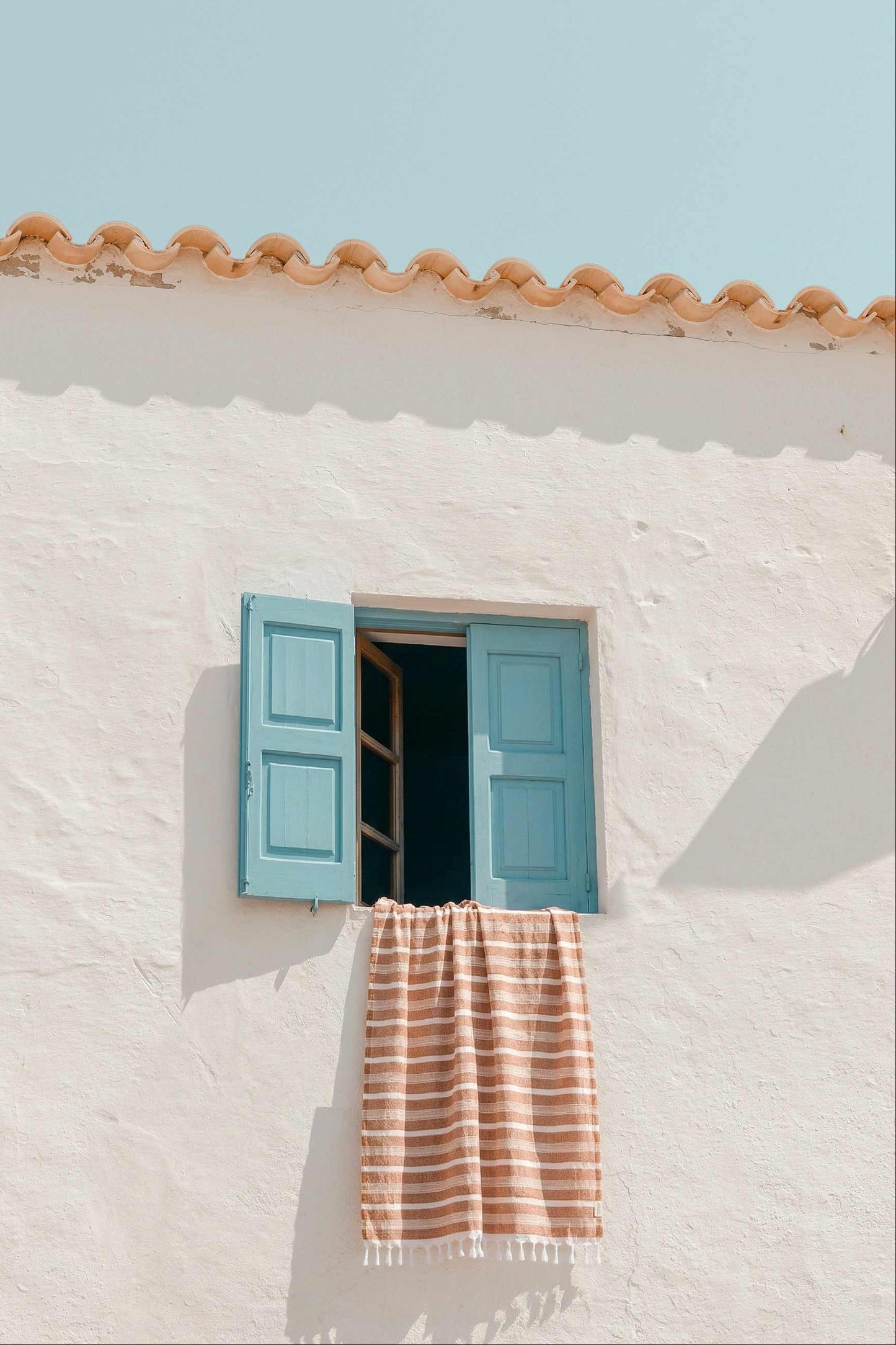 Striped terracotta Turkish towel hanging from blue window on white Mediterranean house, lightweight cotton quick-dry towel for travel, beach, pool, and home