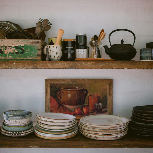 Vintage still life painting displayed on open kitchen shelves with ceramic dishes and pottery, styled as rustic farmhouse kitchen decor.