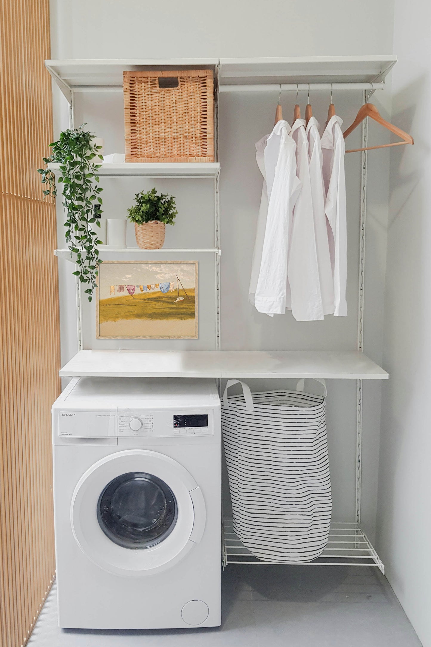 Vintage laundry room wall art above a washing machine in a modern farmhouse laundry room with neutral decor and framed countryside landscape print.
