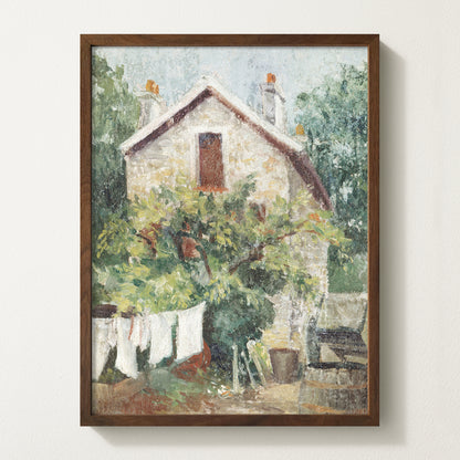 Framed vintage cottage art print featuring a stone house, lush greenery, and white laundry hanging on a clothesline in the garden.