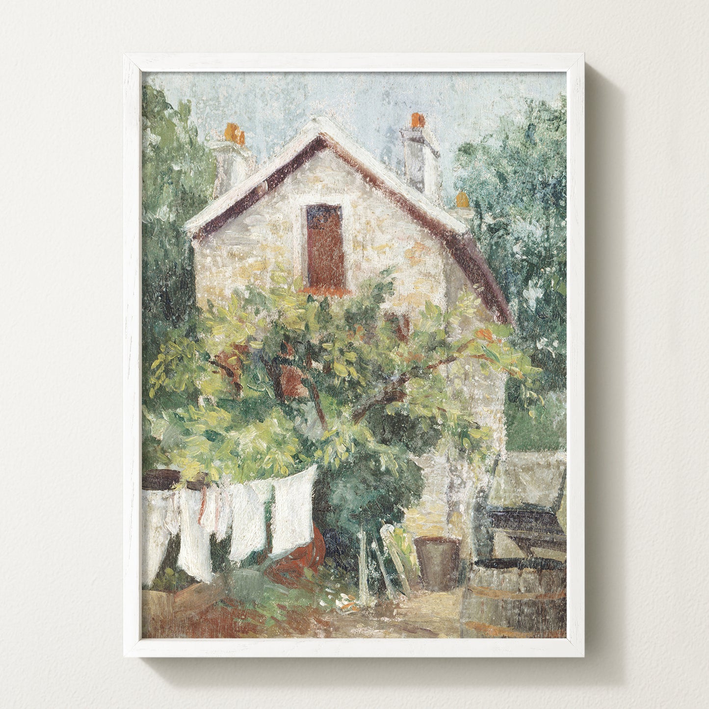 Framed vintage cottage art print featuring a stone house, lush greenery, and white laundry hanging on a clothesline in the garden.