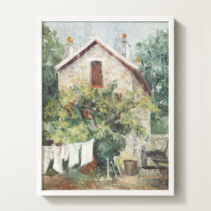 Framed vintage cottage art print featuring a stone house, lush greenery, and white laundry hanging on a clothesline in the garden.