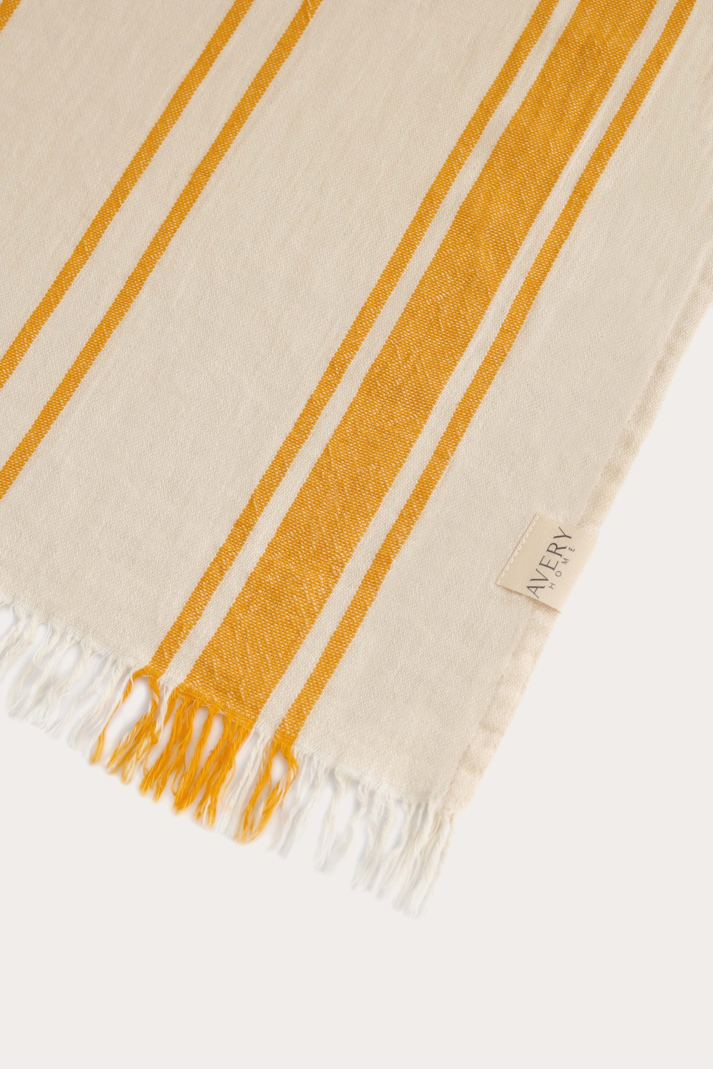 Close-up of yellow and beige Amalfi Turkish towel showing cabana stripe pattern, 100% cotton flat weave texture and fringe by Avery Home.
